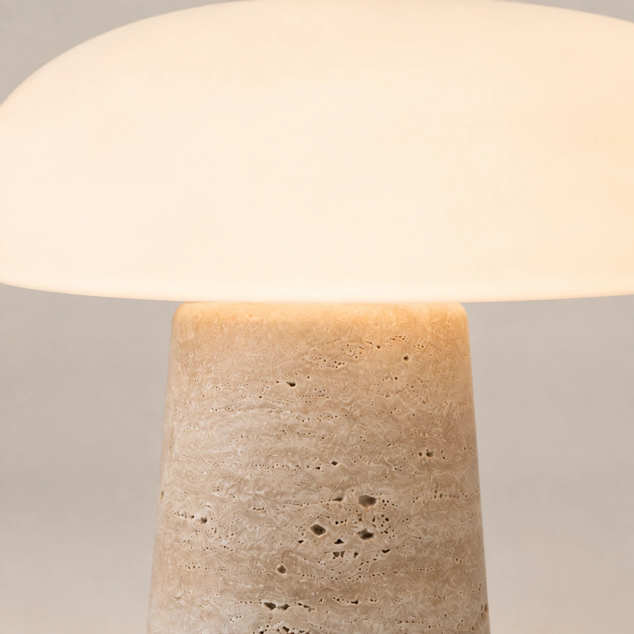 Detalhe do encontro entre o vidro opalino e a base em travertino da Luminária Cala acesa