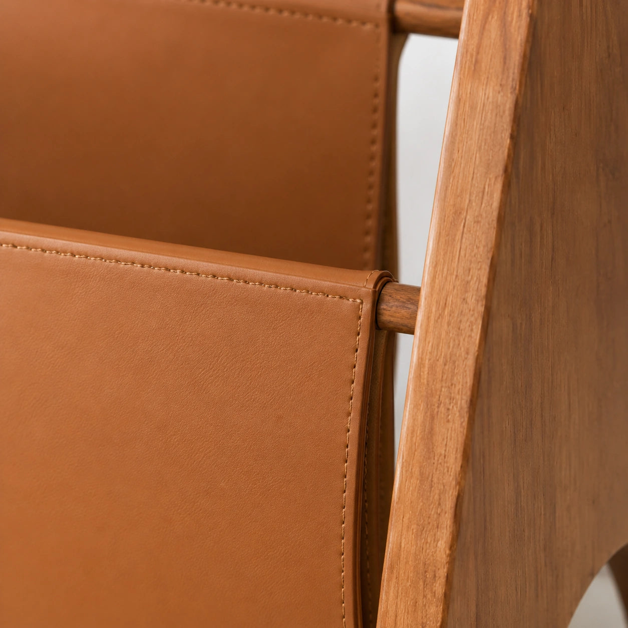 Detalhe do couro caramelo, costura tonal e encaixe na estrutura de madeira do Porta-Revistas Maíra