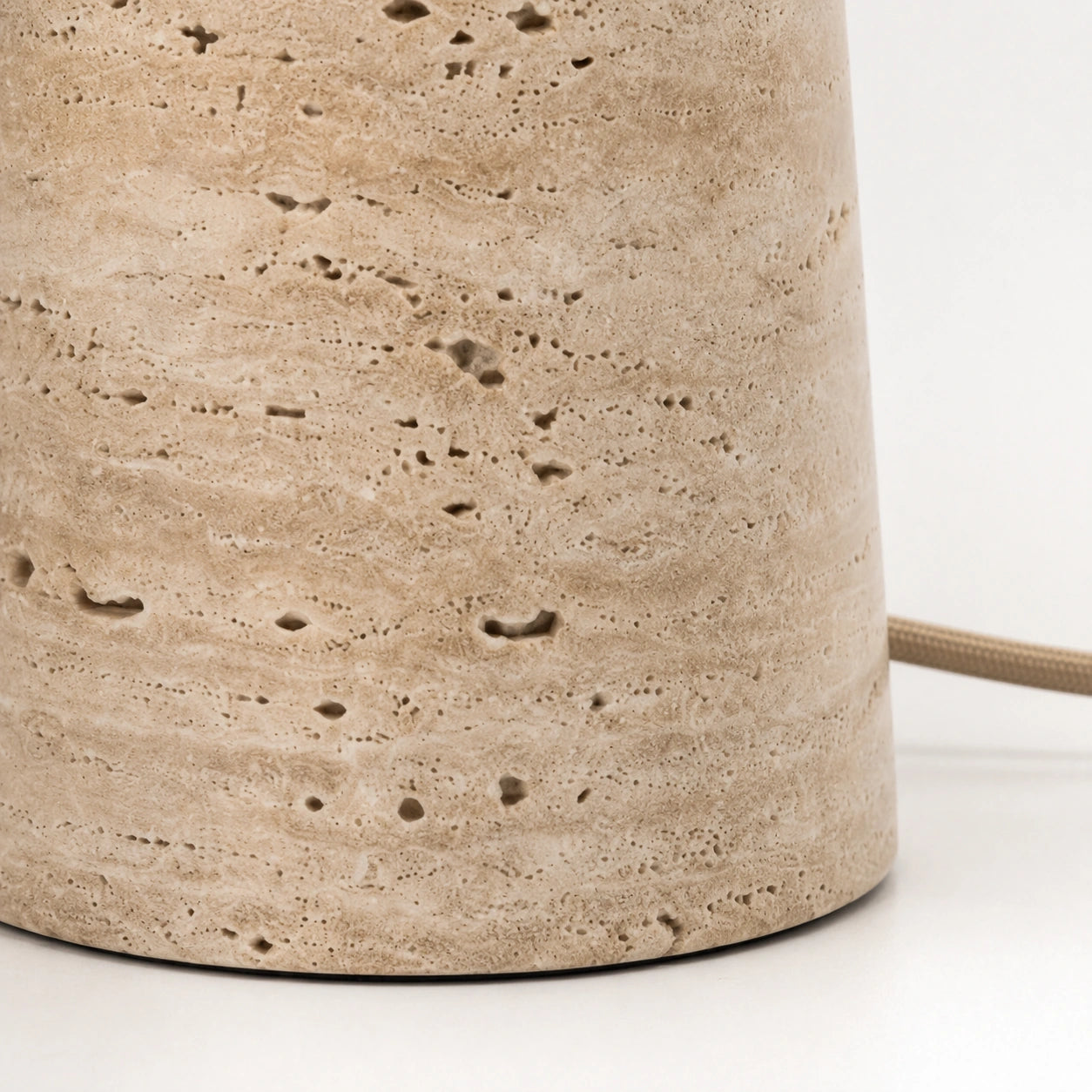 Detalhe dos veios, poros e textura natural da base em travertino da Luminária Cala