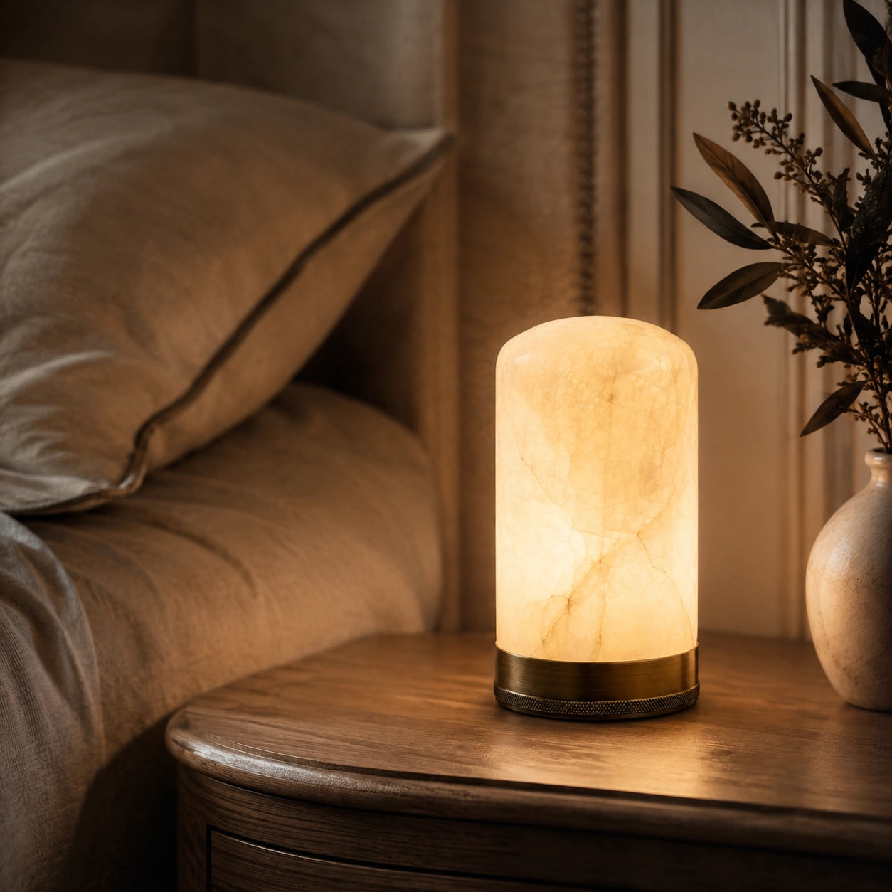 Luminária Portátil Éloise acesa sobre mesa de cabeceira em quarto elegante